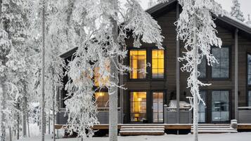 A wooden cabin with multiple windows and a porch, surrounded by snow-covered trees.