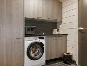 Un espace buanderie compact comprenant un lave-linge à chargement frontal, une petite poubelle et des placards en bois.
