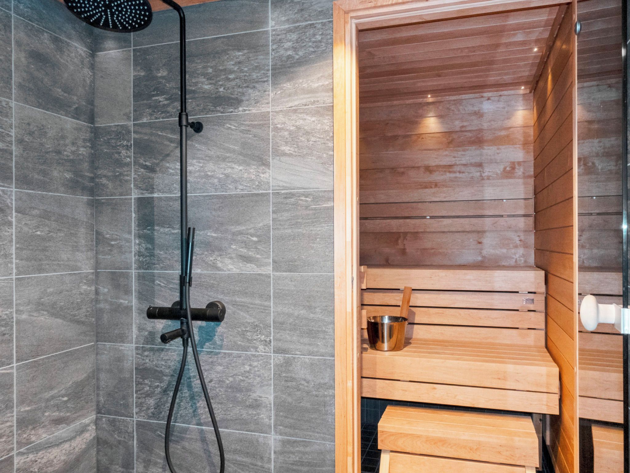 A shower area with a wooden bench and a metal bucket.