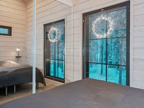 Une chambre à coucher moderne, avec un lit, une table de chevet et une lampe. On y trouve deux portes dotées de fenêtres en verre dépoli, chacune ornée d’une guirlande illuminée.
