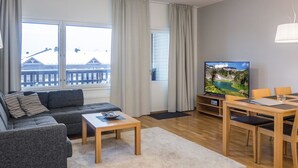 A modern living room with a sofa, coffee table, TV, and dining area. - Ruka ski chalets 64, 1302 by Interhome (Kuusamo)