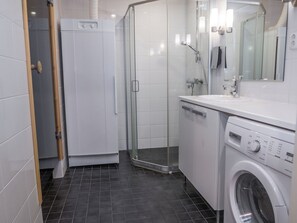 A modern bathroom with a glass shower enclosure, a built-in washing machine, and a sink with a mirror. - Ruka ski chalets 64, 1302 by Interhome (Kuusamo)