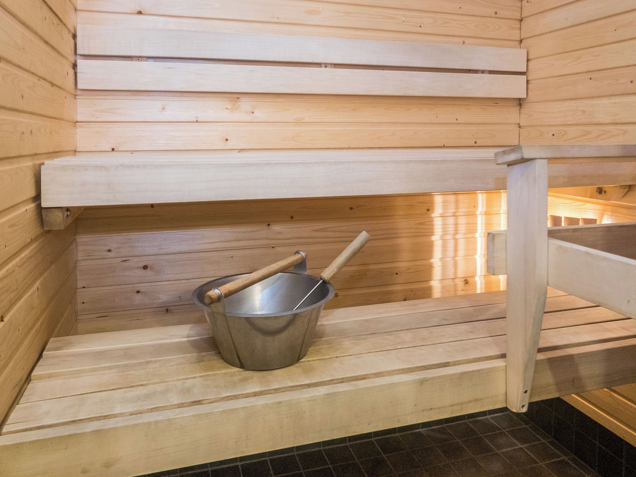 Un sauna avec des bancs en bois et un seau en métal doté d’un manche en bois.