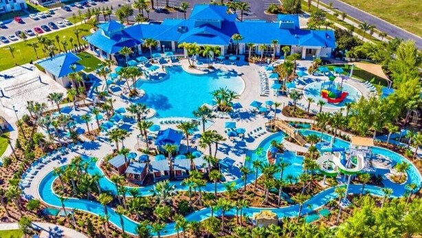 Et resort med en central pool, flere loungeområder og en bygning med et blåt tag.