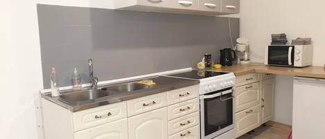 A modern kitchen with white cabinetry, a stainless steel sink, a stove, and a microwave.