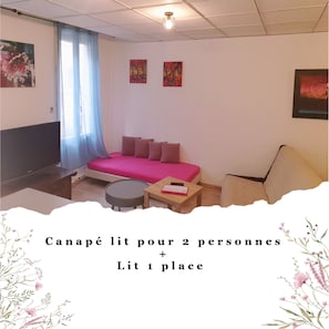 Ein Zimmer mit einem Bett, einem Sessel, einem kleinen Tisch und Bildern an den Wänden.