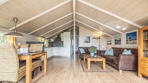 Un loft espacioso con techos altos, un comedor con mobiliario de mimbre, una sala de estar con un sofá marrón y una mesa de centro, y una cocina al fondo.