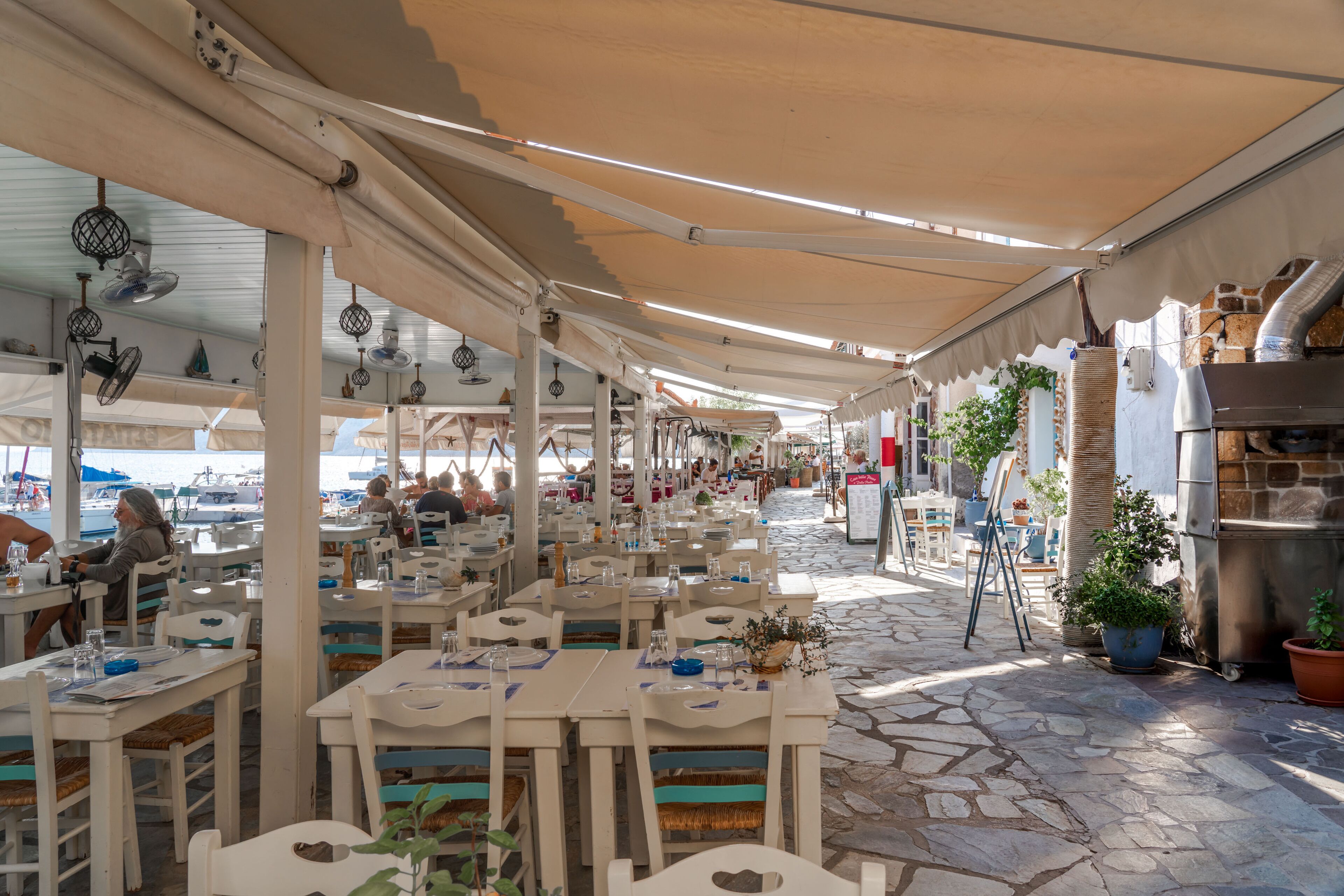 An outdoor dining area with tables and chairs, a stone floor, and a covered walkway.