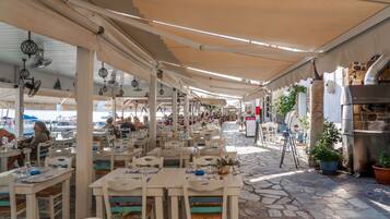 An outdoor dining area with tables and chairs, a stone floor, and a covered walkway.