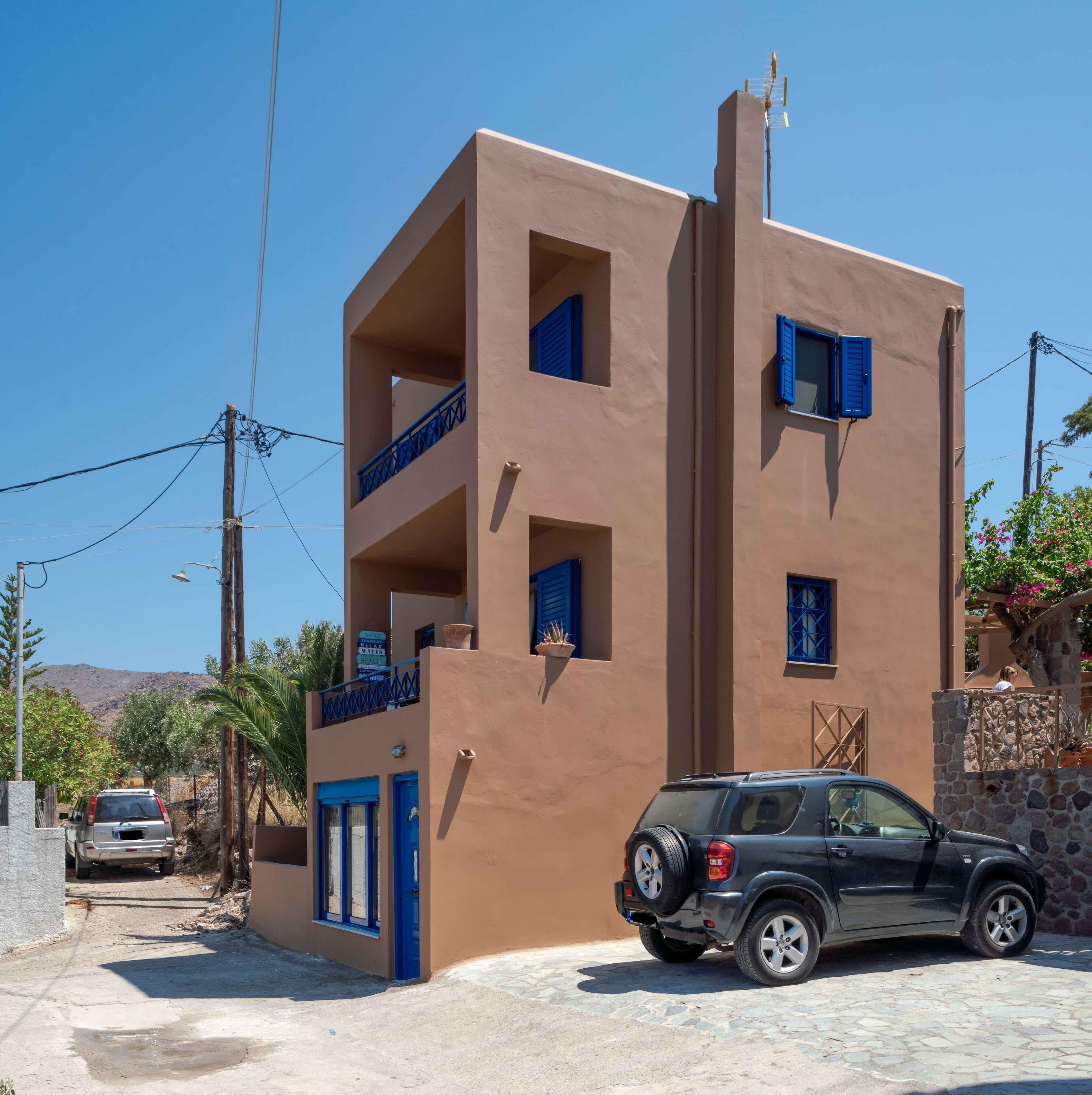 Un edificio de varios pisos con contraventanas azules y un coche estacionado adelante.