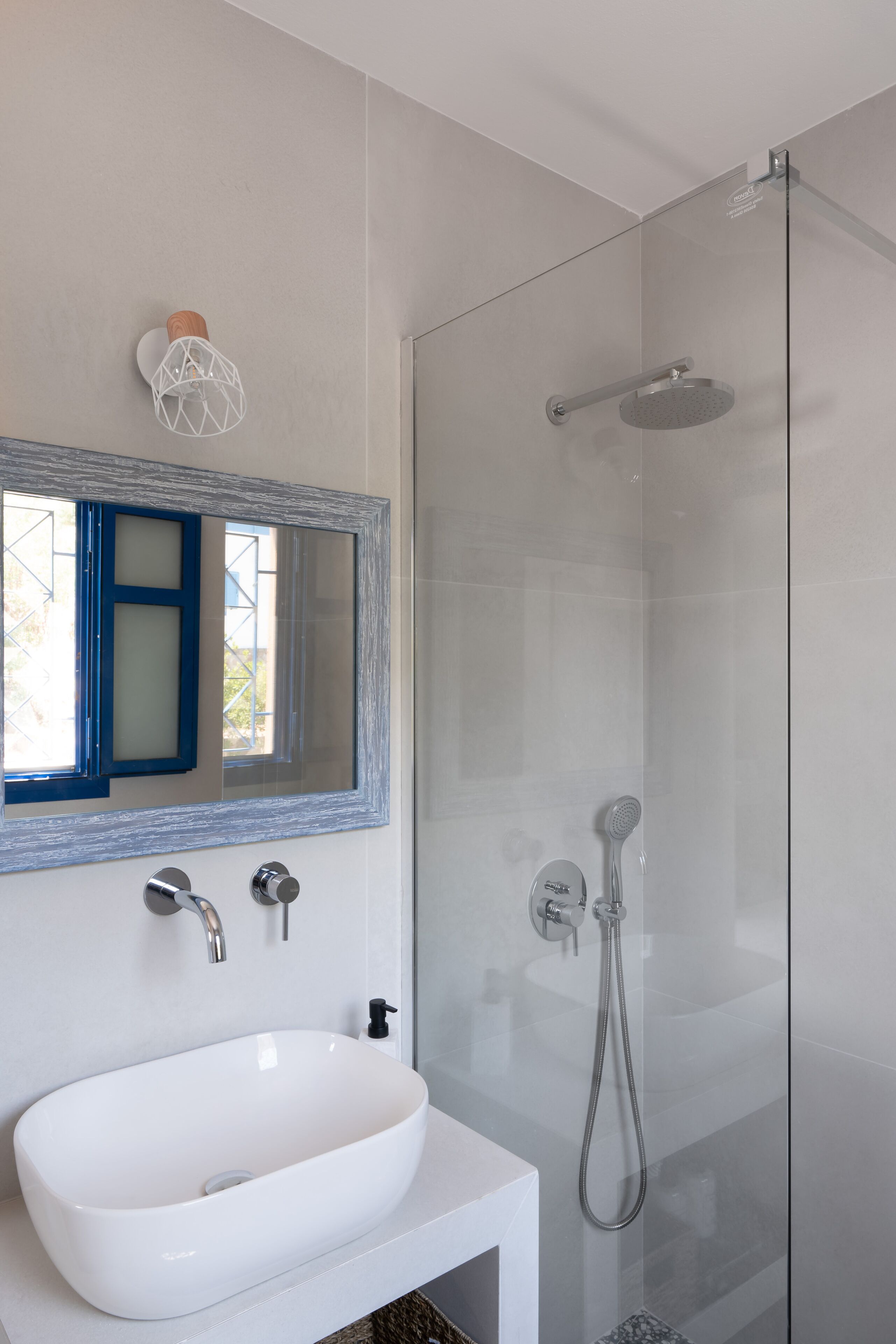 A modern bathroom with a white sink, a glass shower enclosure, and a mirror with a blue frame.