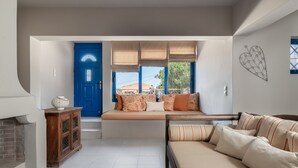 Una sala de estar con una puerta azul, un sofá con cojines estampados, un armario de madera y una pared con diseño geométrico.