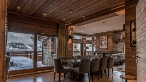 A spacious dining area with a wooden ceiling, large windows, and a view of snow-covered mountains. - Luxurious Ski-in/Ski-out Apartment with Jacuzzi and Private Hammam (Méribel)