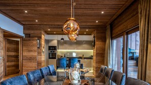 A modern dining area with a wooden ceiling, a glass-top table, and blue upholstered chairs. - Luxurious Ski-in/Ski-out Apartment with Jacuzzi and Private Hammam (Méribel)