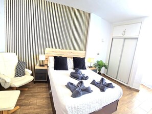 Habitación de hotel con una cama grande, una mesita de noche con lámpara, una silla, un armario y una pared a rayas verticales.