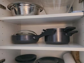Una repisa en la cocina con un colador, una olla con tapa y una pila de tapas negras.