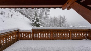 Un balcon enneigé, doté d’une balustrade en bois, d’où l’on peut admirer un paysage hivernal avec des arbres couverts de neige.