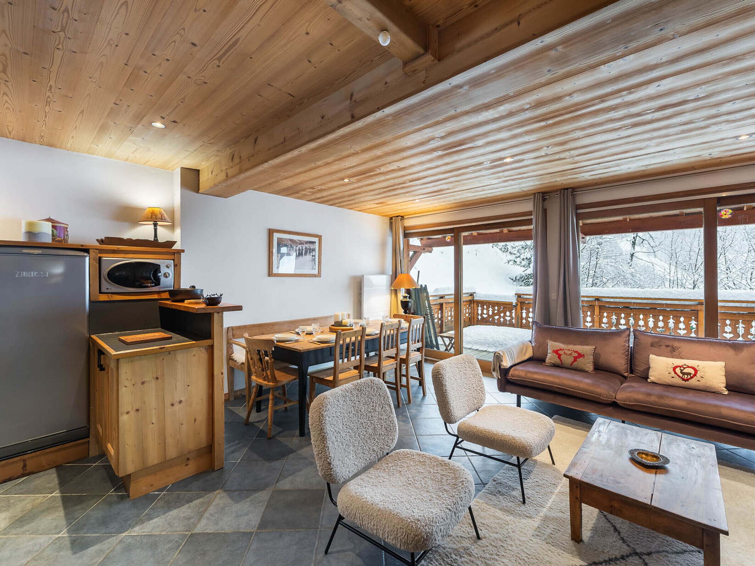 L’intérieur chaleureux d’un chalet comprend un coin repas en bois, un canapé et une cuisine équipée d’un réfrigérateur et d’un four à micro-ondes.