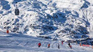Une piste de ski avec des skieurs, un télésiège et un paysage montagneux en arrière-plan.