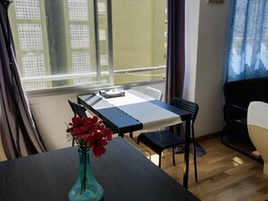 Ein Zimmer mit Tisch, Stühlen, einer Vase mit Blumen und Blick auf Gebäude durch das Fenster.