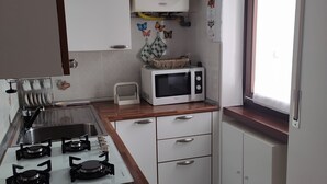 Cocina compacta con estufa a gas, microondas y gabinetes blancos.