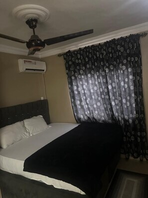 Une chambre à coucher avec un lit, un ventilateur de plafond, un appareil de climatisation et un rideau à motifs à pois.
