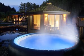 Un jacuzzi rodeado por un pabellón de madera con vista a una casa y un estanque.