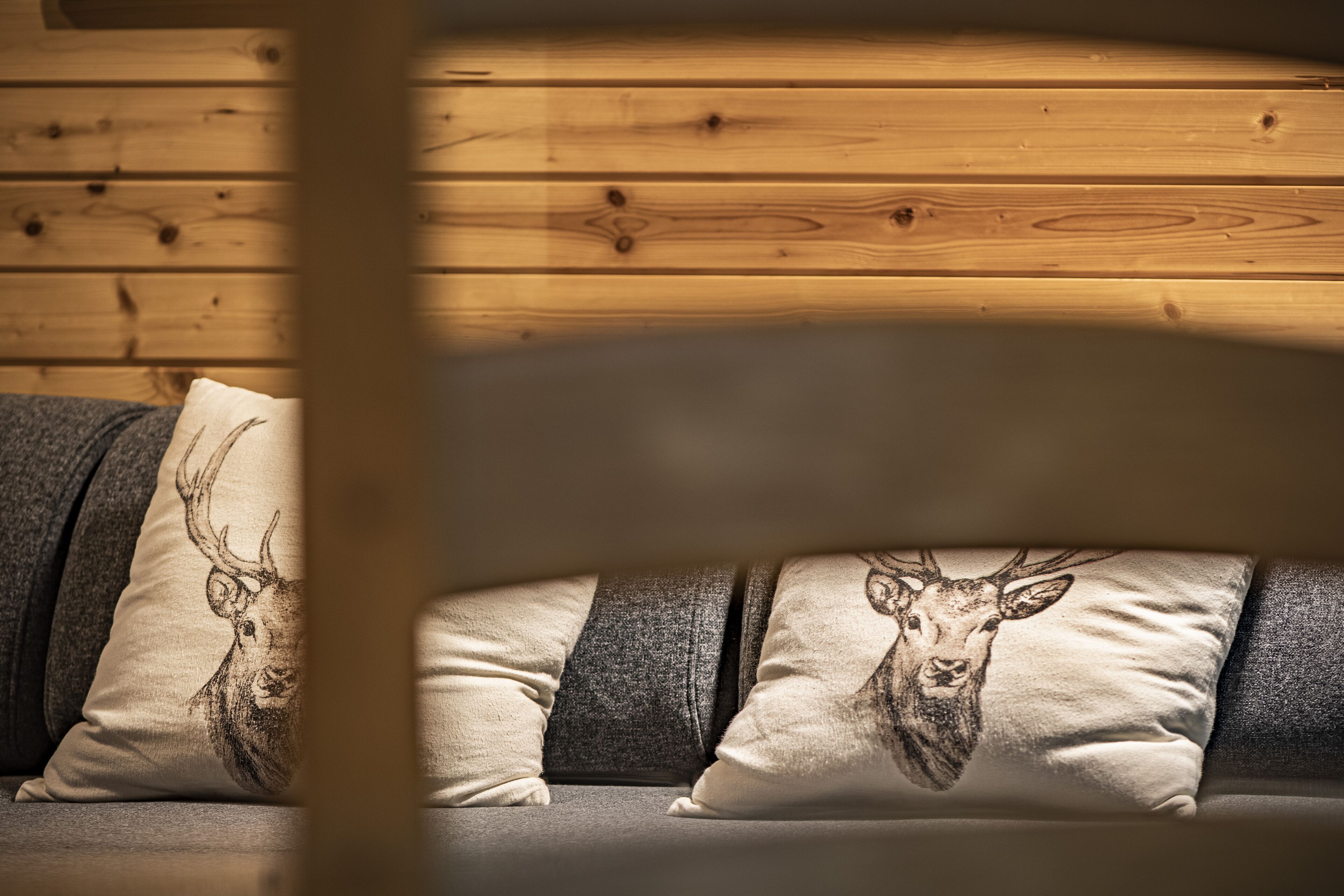 A sofa with patterned cushions against a wooden wall.