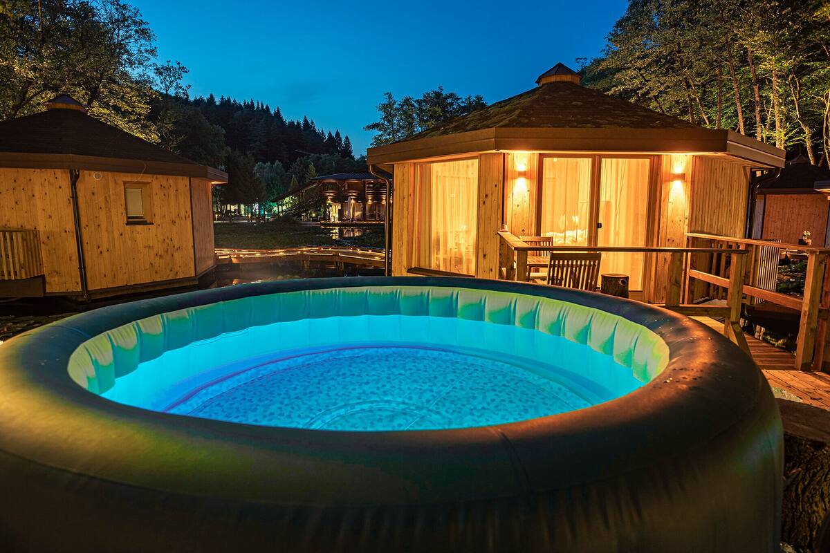 A hot tub surrounded by wooden cabins with a view of a forested area.