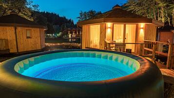 A hot tub surrounded by wooden cabins with a view of a forested area.