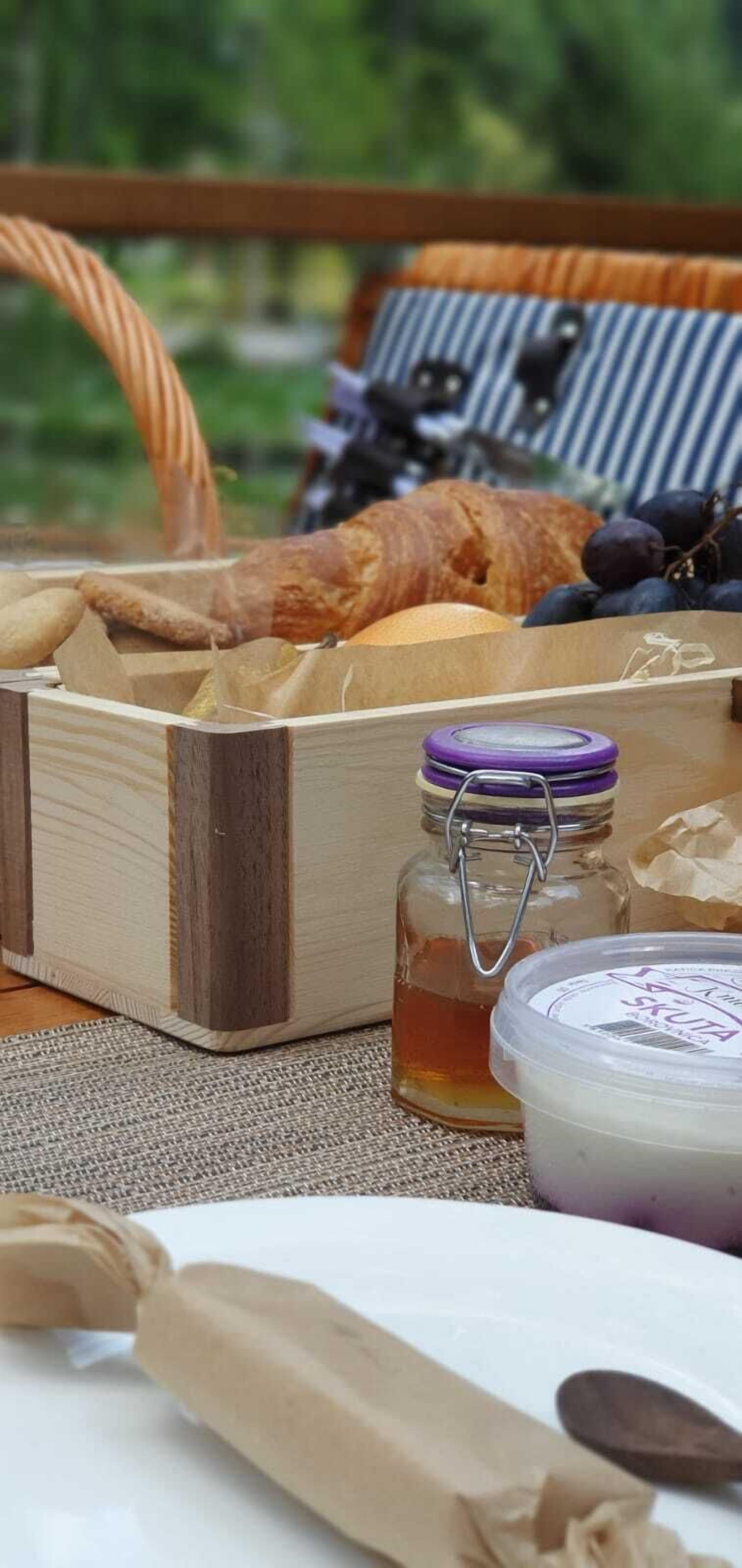 Ein Picknicktisch mit einem Korb, der Brot, ein Glas Honig und eine Joghurt-Behälter enthält.
