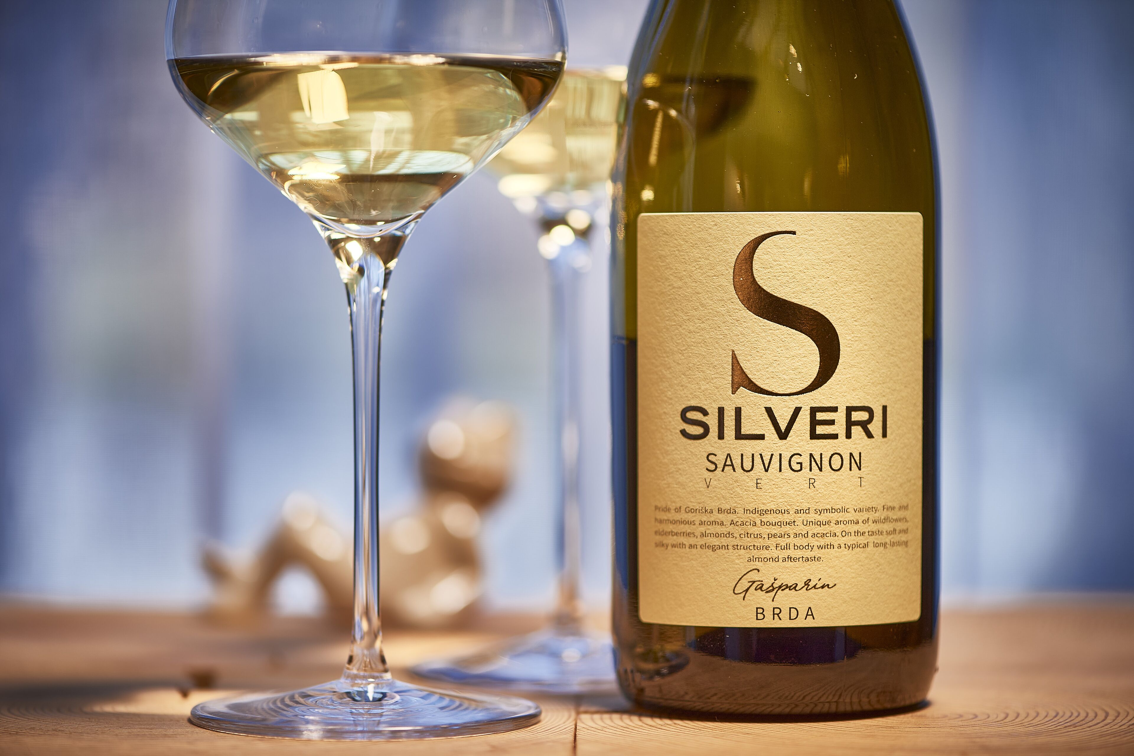 Una botella de Sauvignon Blanc Silveri y una copa de vino sobre una superficie de madera.