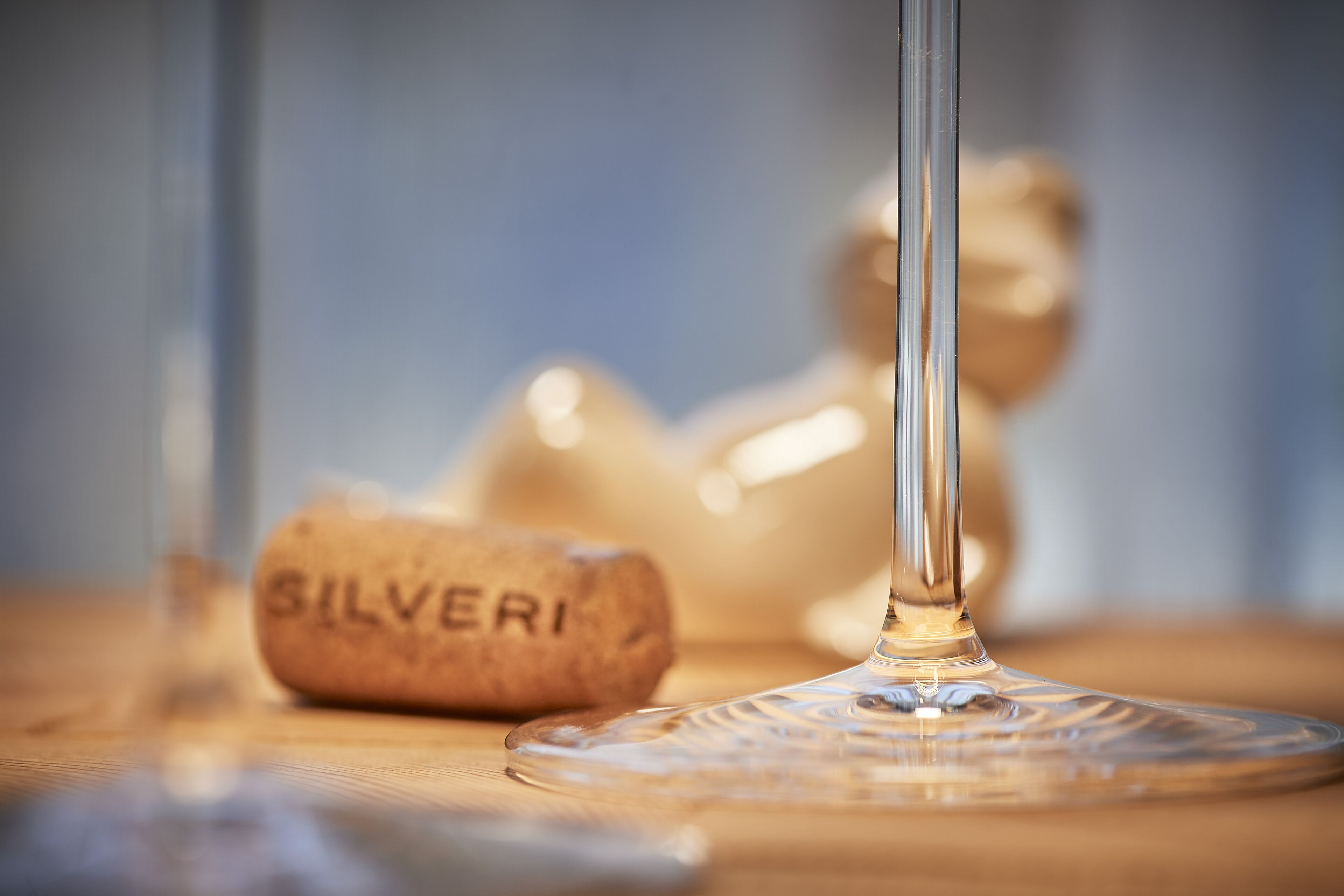A clear glass wine glass with a cork labeled "SILVERI" and a blurred background.