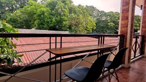 A balcony with a table and chairs, overlooking a red-roofed building and lush greenery. - Ginto Residence (Coron)