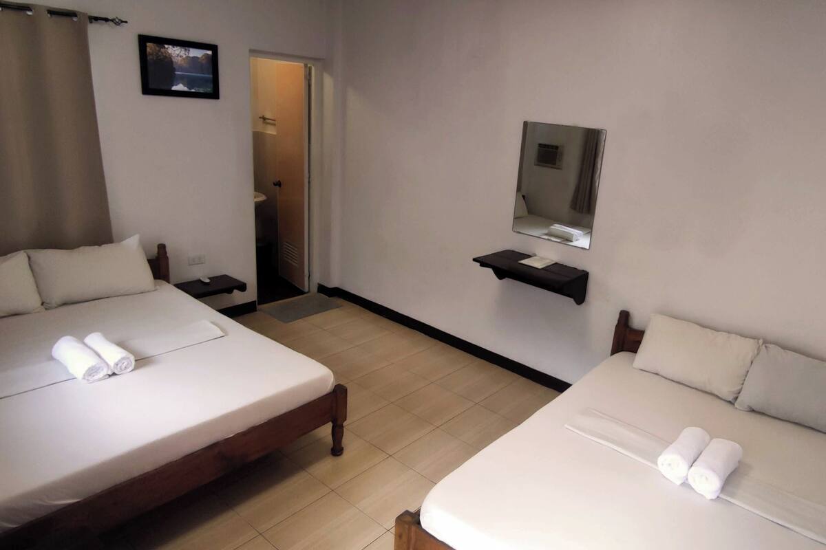 A hotel room with two beds, a bathroom, a mirror, and a door leading to another room.