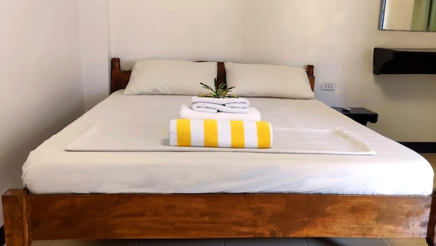 A neatly made bed with white linens, a yellow and white striped towel, and a small plant. - Ginto Residence (Coron)