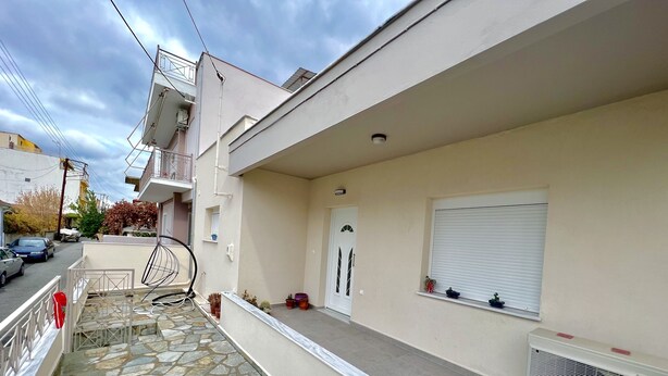 A residential building with a stone-paved balcony, a white door, and a window with blinds.