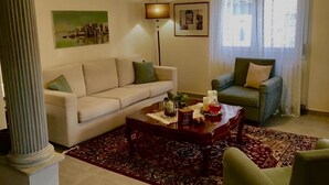 A living room with a sofa, armchair, coffee table, and a large window with curtains.