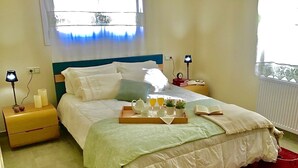A neatly made bed with a tray of breakfast items, a bedside table with a lamp, and a window with curtains.