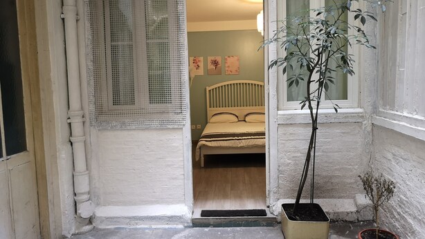 Un couloir étroit mène à une chambre qui contient un lit, une fenêtre et une plante en pot.