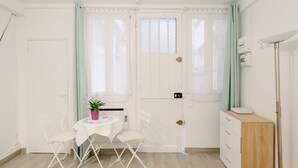 Une petite pièce lumineuse avec une porte blanche, une table entourée de chaises, une petite plante et un meuble en bois.