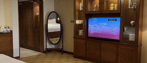 A hotel room with a large bed, a chandelier, a television, and a wooden cabinet with glass doors.