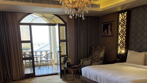 A spacious hotel room with a large bed, a chandelier, a balcony with chairs, and a view of the outside. - AL Rahden Hotel  (Riyadh)