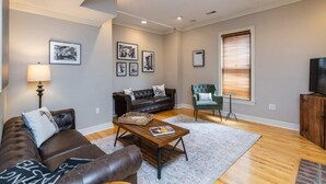 A living room with a brown leather sofa, a green armchair, a wooden coffee table, and a television on a wooden cabinet. - This house is a 3 bedroom(s), 2.5 bathrooms, located in Lexington, KY. (Lexington)