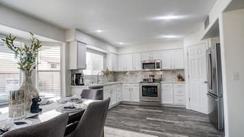 Una cocina moderna con armarios blancos, una zona de comedor con una mesa para cuatro personas y un amplio ventanal que proporciona luz natural.