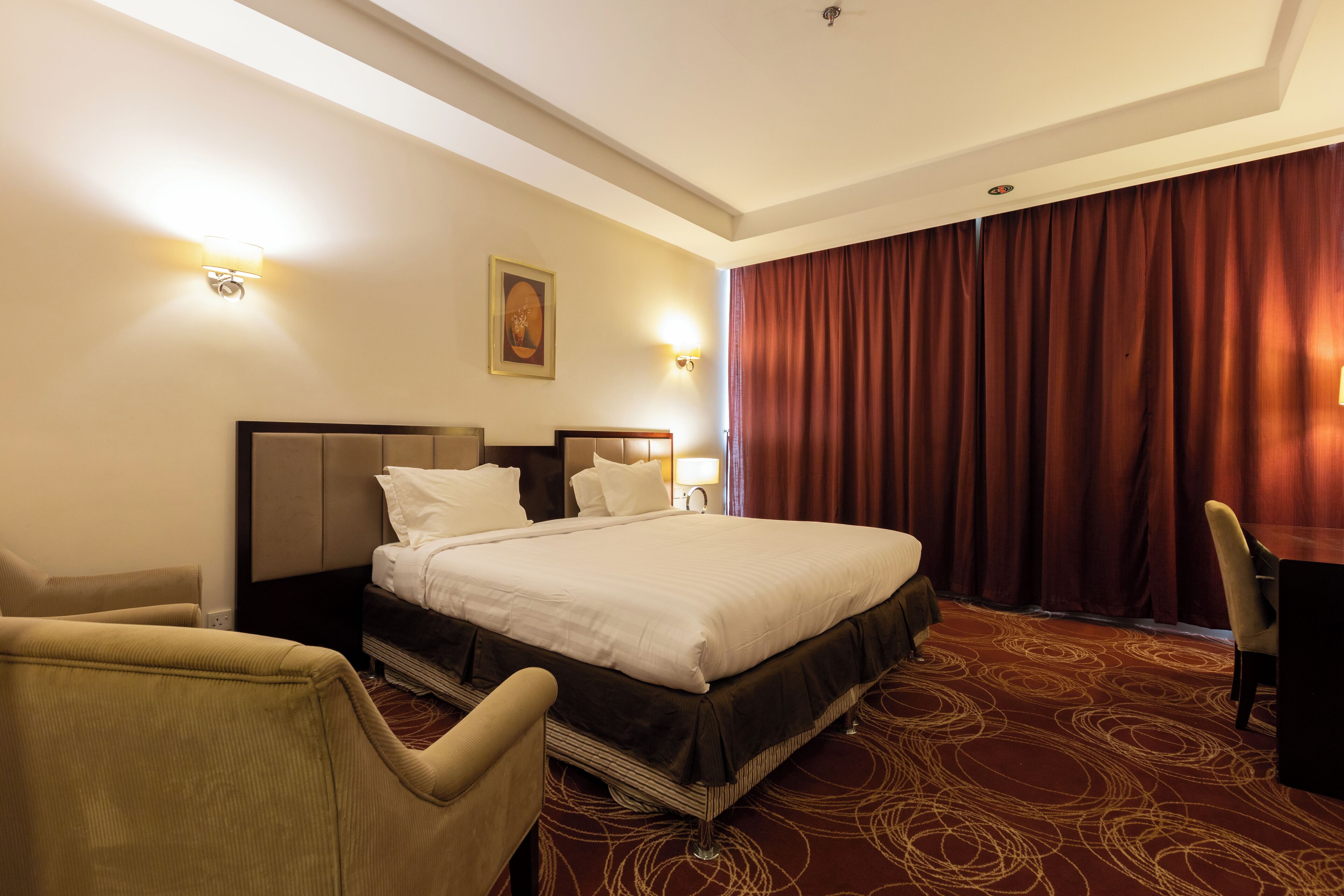 Una habitación de hotel con una cama grande, dos mesitas de noche, una silla y suelo alfombrado.