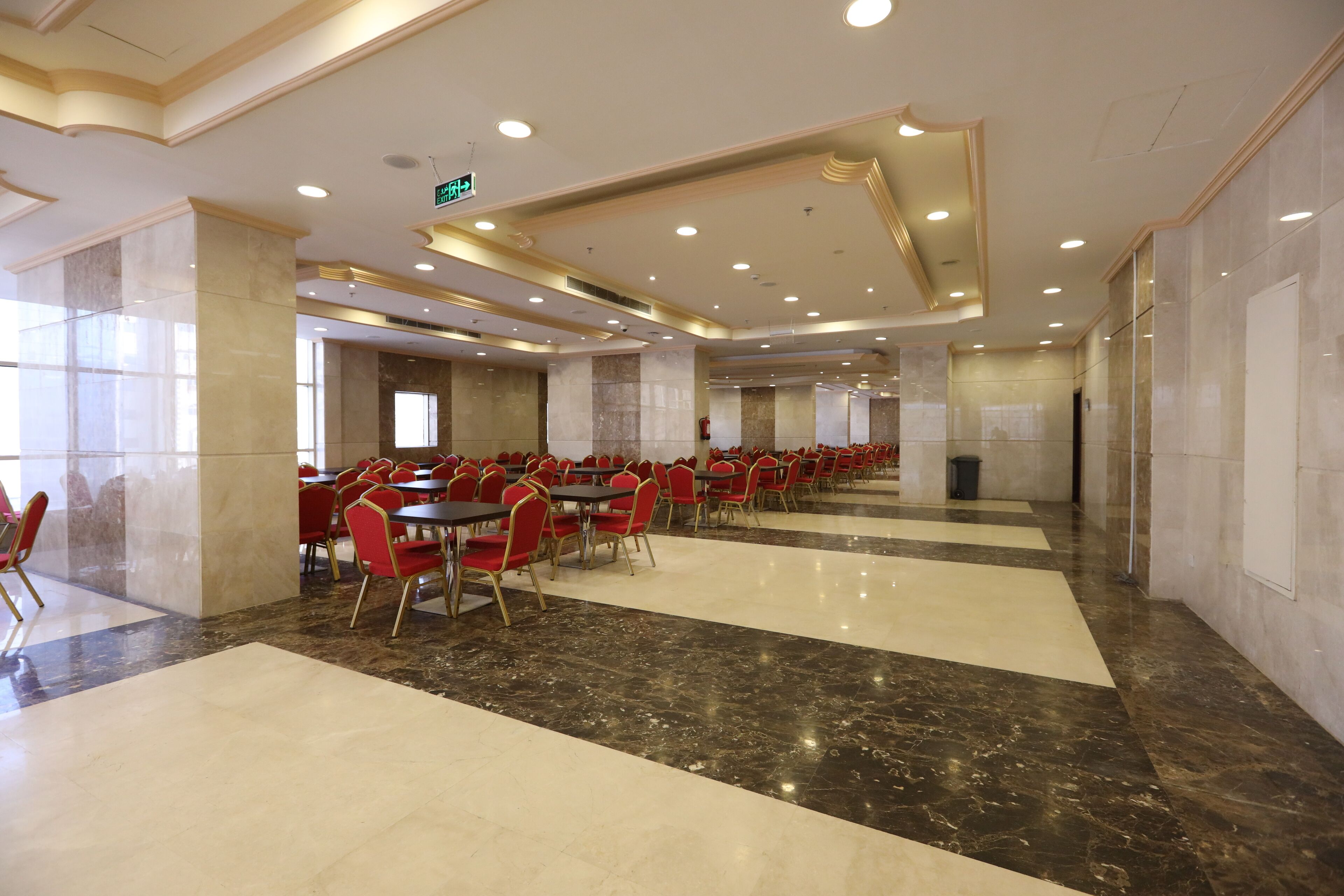 A spacious indoor dining area with marble flooring, red chairs, and tables arranged in rows.
