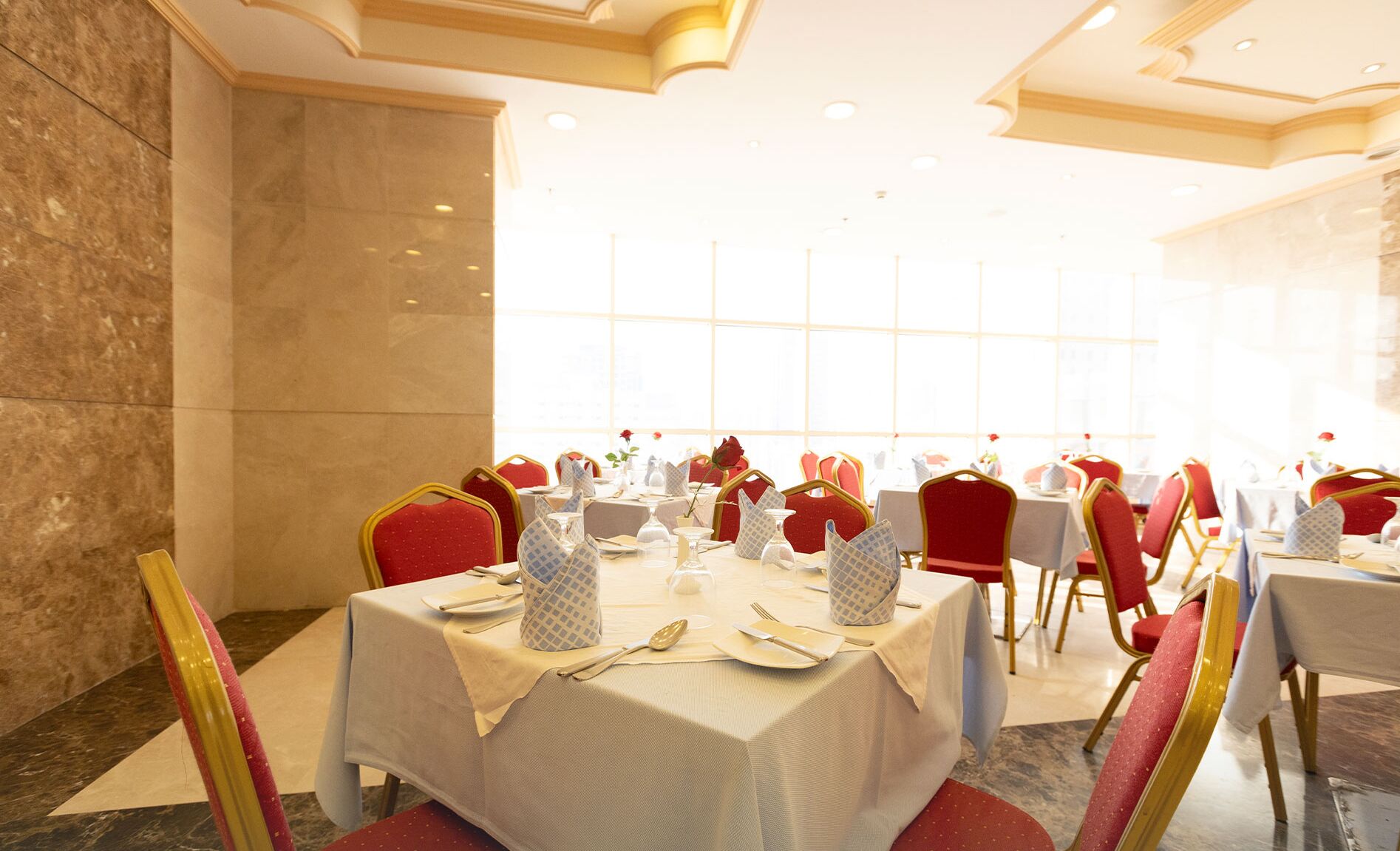 A dining area with tables set for service, red chairs, and a marble wall.