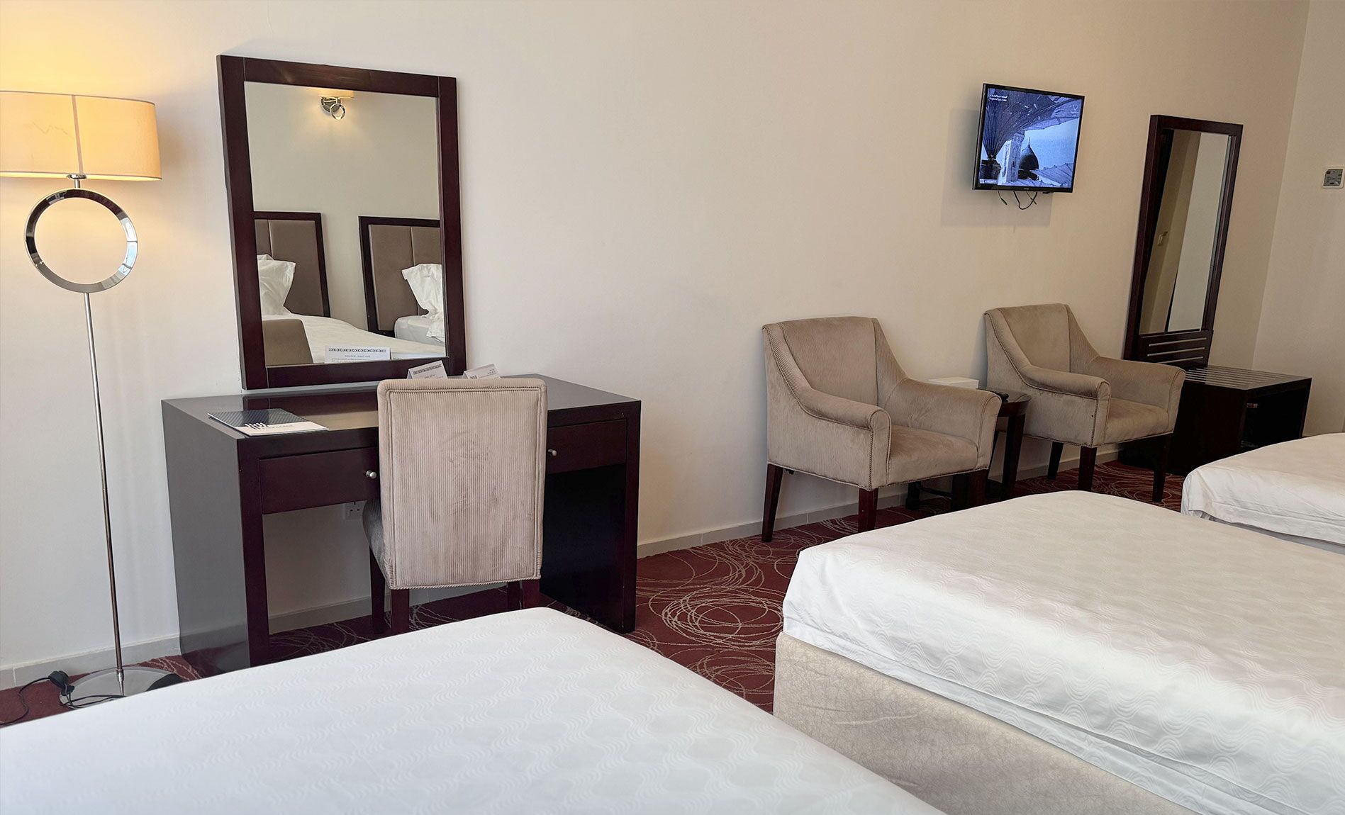 Een hotelkamer met twee bedden, een bureau met stoel, een televisie en een spiegel.