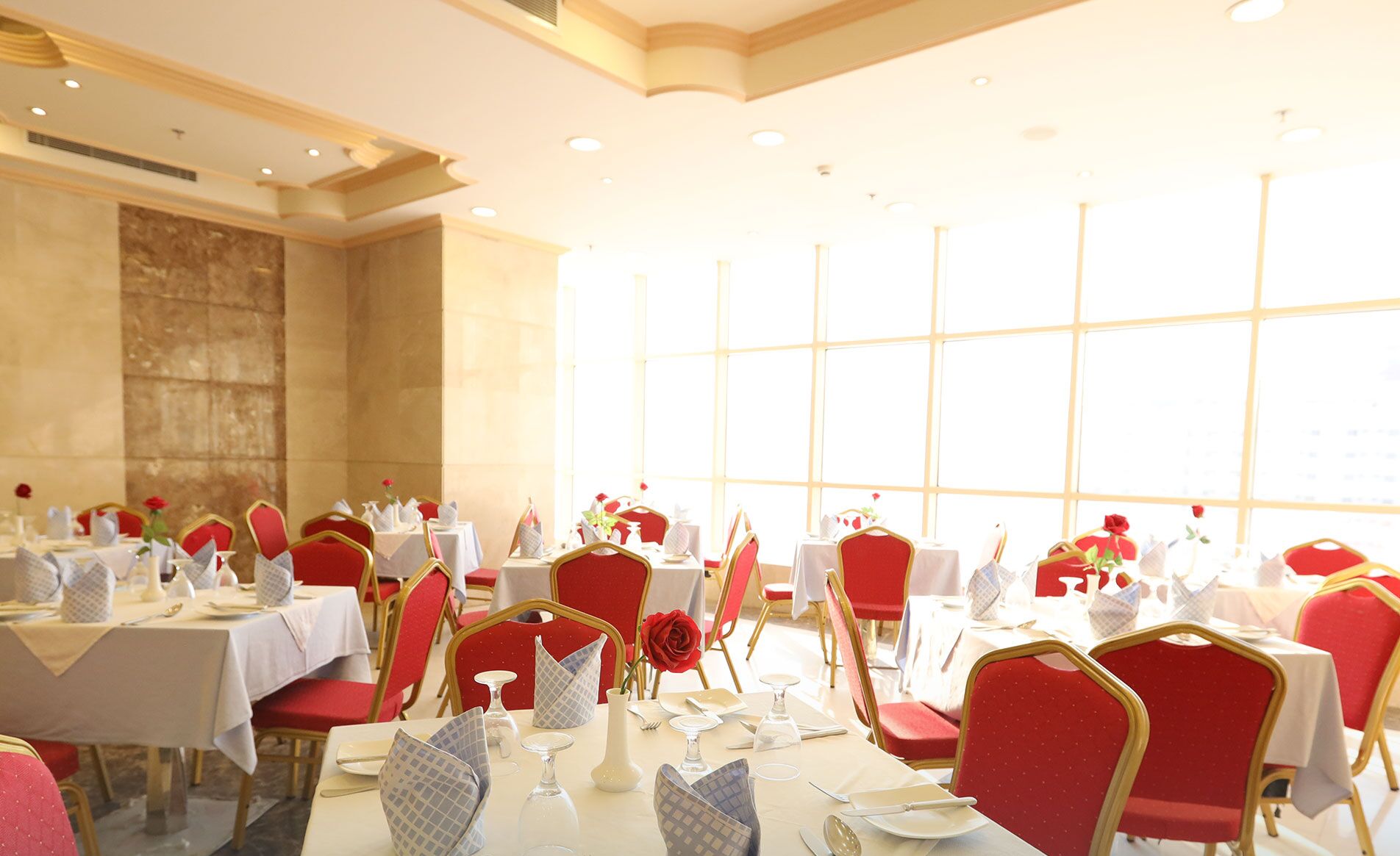 A well-lit dining area with tables set for service, featuring red upholstered chairs and white tablecloths.